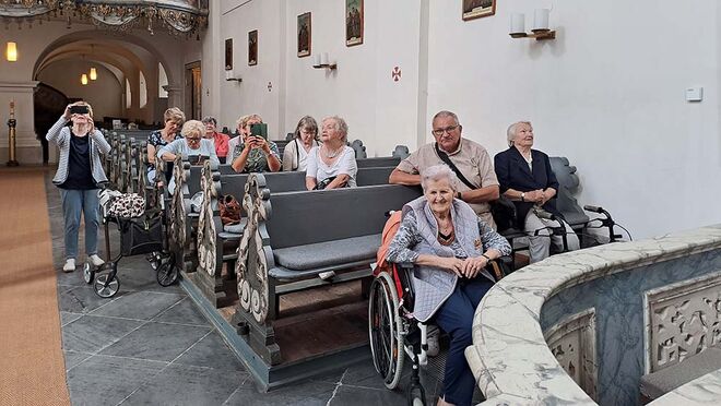 Ältere Menschen sitzen in Kirchenbänken und bestaunen den Kirchenbau um sich herum.