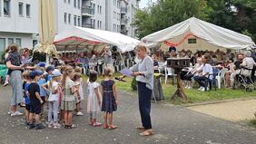 Eine Gruppe kleiner Kinder führt ein Programm auf. Senioren sehen zu.