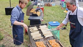 Zwei Männer stehen an einem Grill und bereiten etwas zu essen zu.